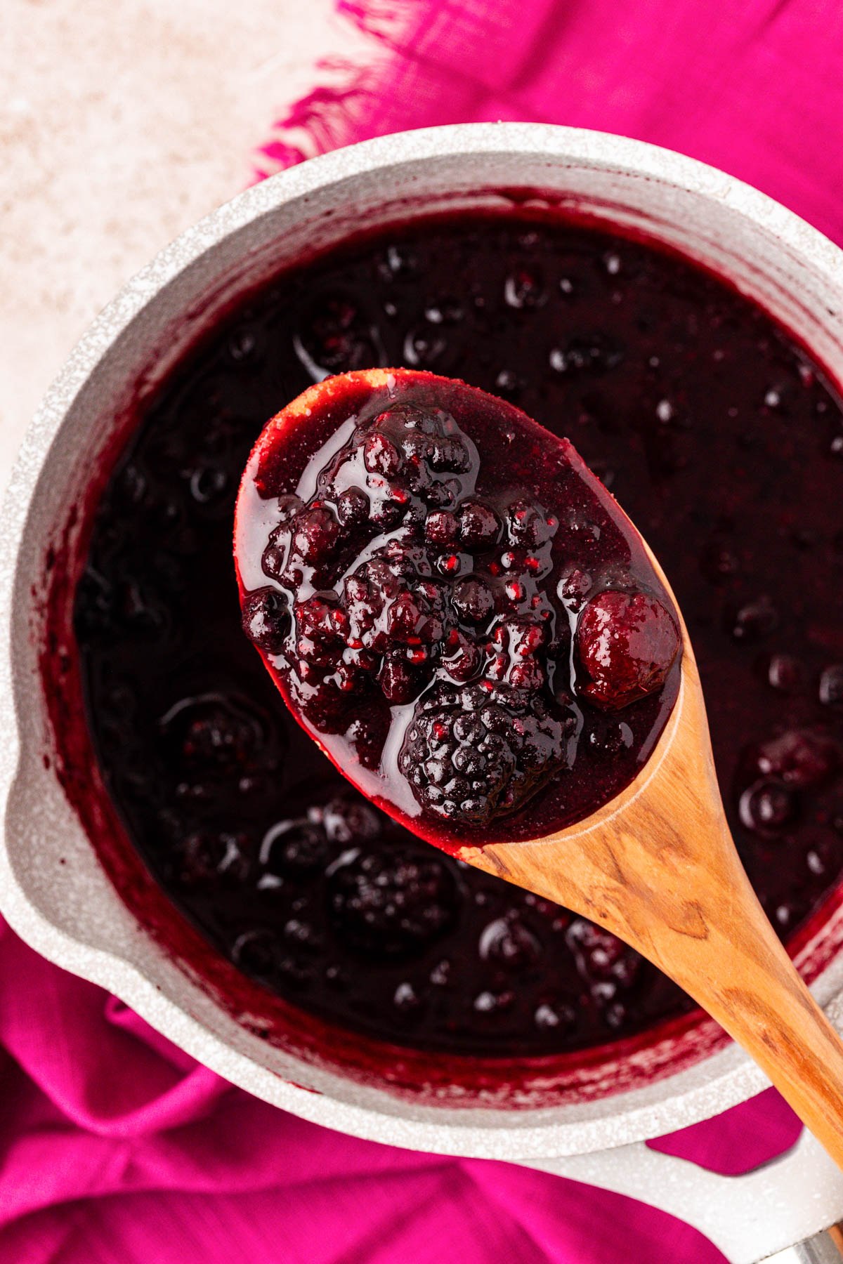 A serving spoon with mixed berry compote over a pot.