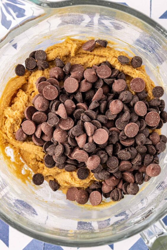 Chocolate chips being added to cookie dough in a mixing bowl.