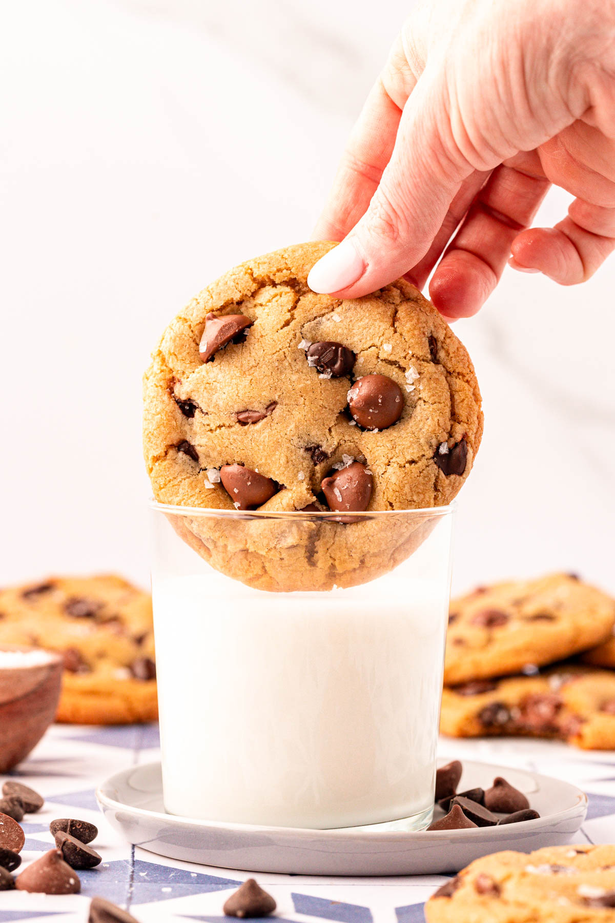 A woman's hand dipping a bakery style chocolate chip cookie into a glass of milk.