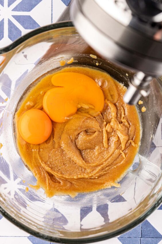 Eggs being added to wet ingredients in a mixing bowl.