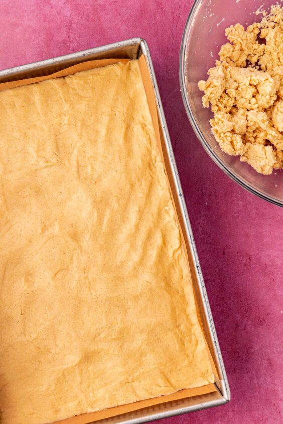 Shortbread dough being spread in the bottom of a 9x13-inch pan.