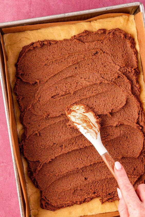 Cinnamon filling being spread over cookie dough in a pan.