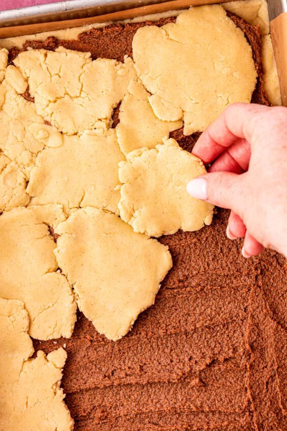 A woman's hand adding dough to shortbread cookie bars with cinnamon filling.