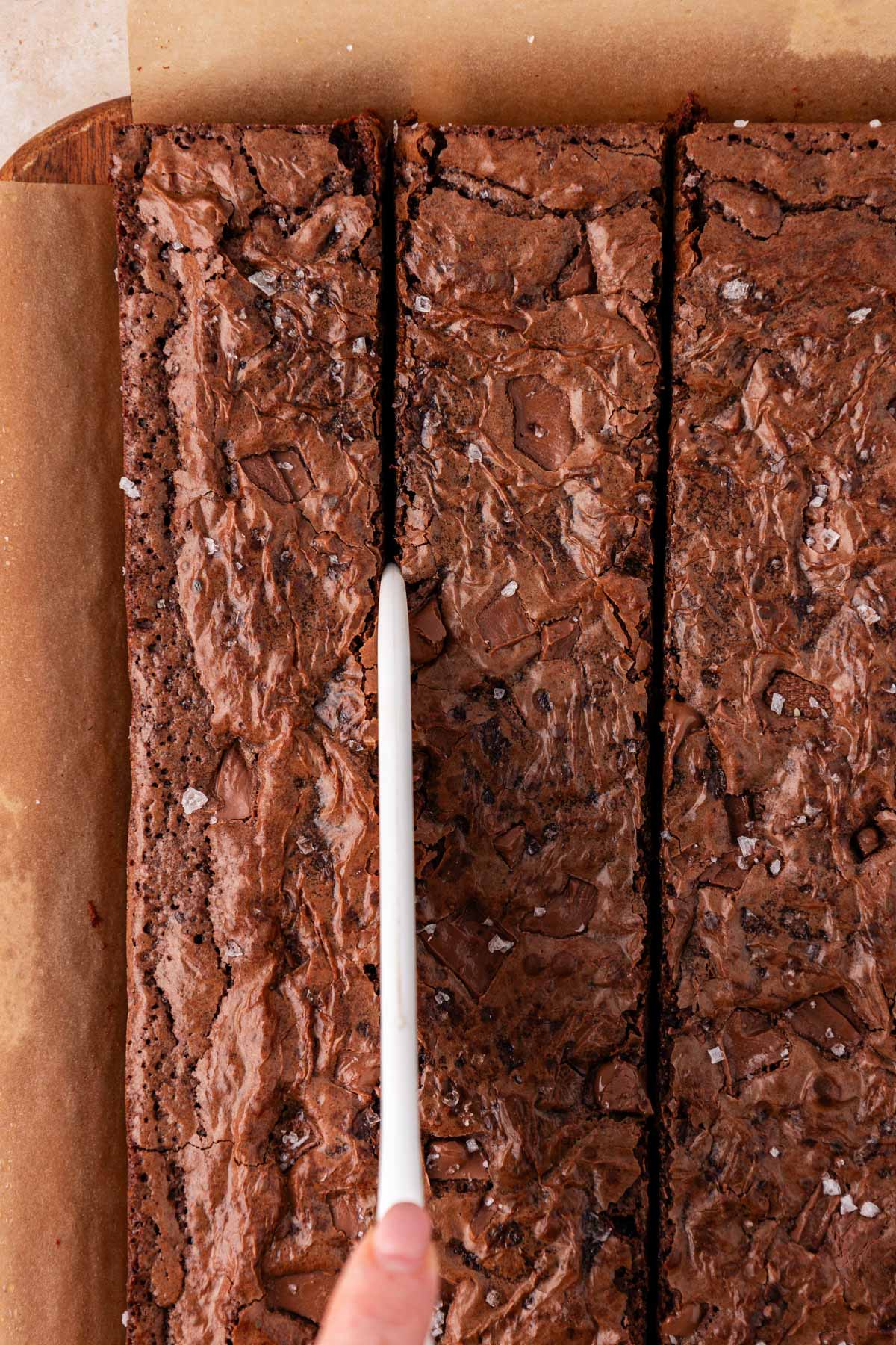 Overhead shot of brownies being cut with a large plastic knife.