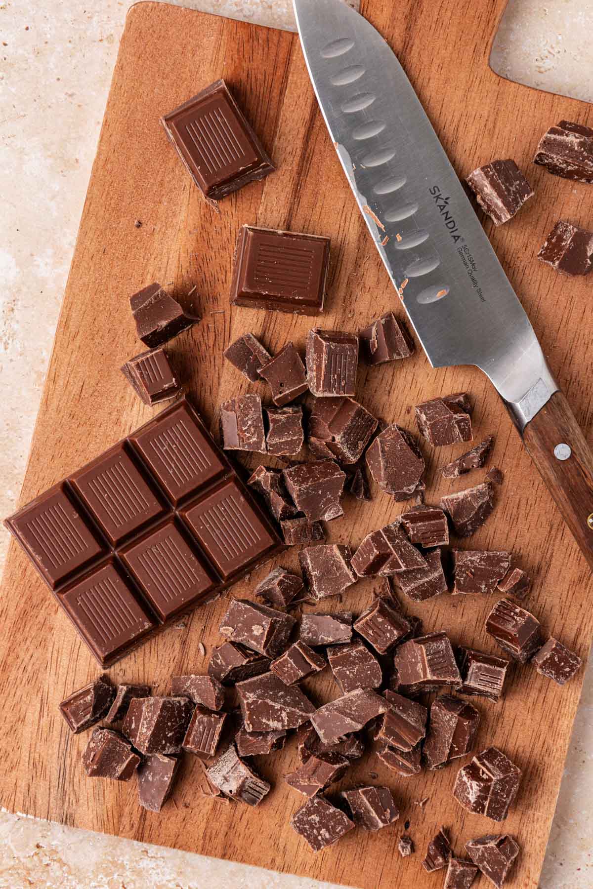 Chopped chocolate on a cutting board with a knife.