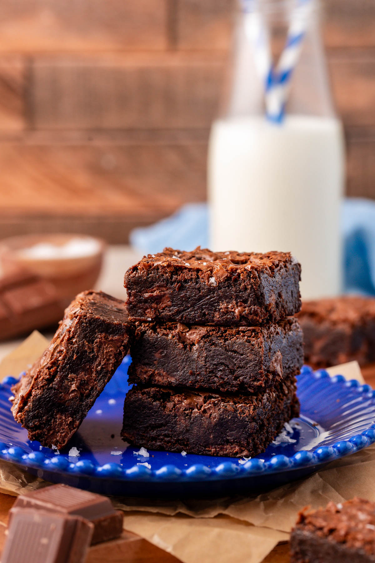 A stack of three brownies on a blue plate with another brownie leaning against them.