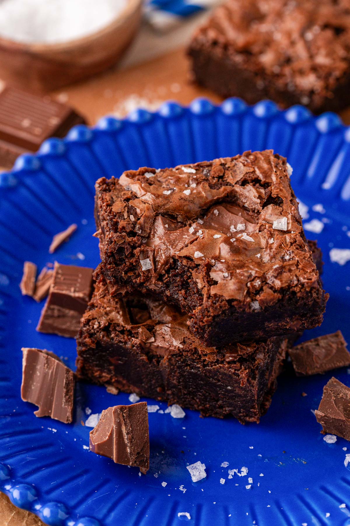 Two chocolate fudge brownies on a blue plate, one is missing a bite.