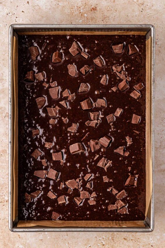 Chocolate chunk brownie batter in a 9x13-inch pan ot a table.