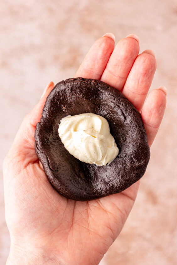 Cheesecake cookie filling in chocolate cookie dough in a woman's hand.