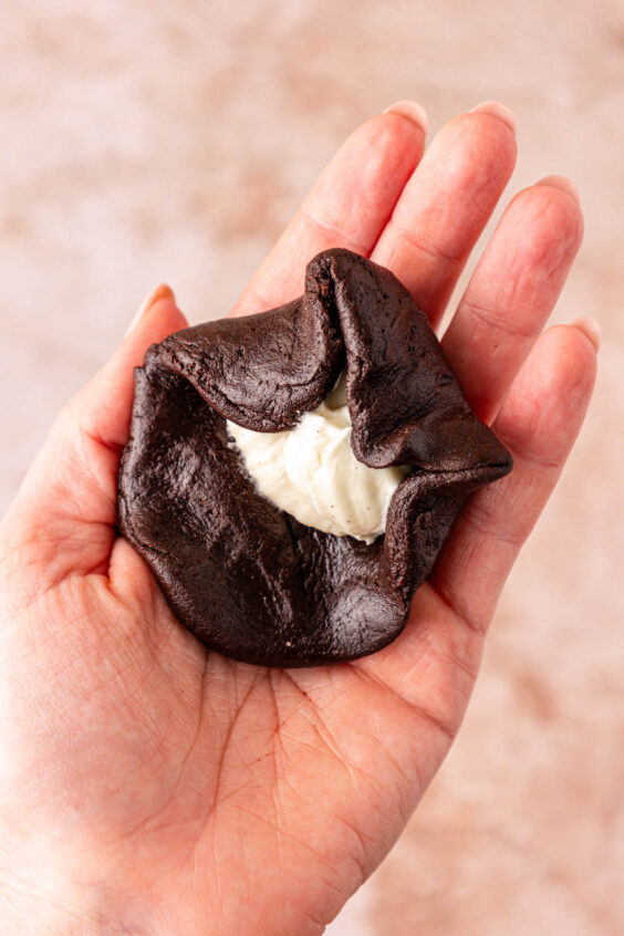 Chocolate cookie dough being wrapped around cream cheese in a woman's hand to make cookies.