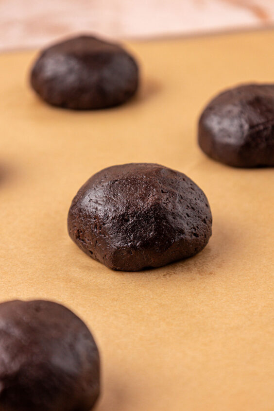 Chocolate cookie dough balls on a parchment lined baking sheet.