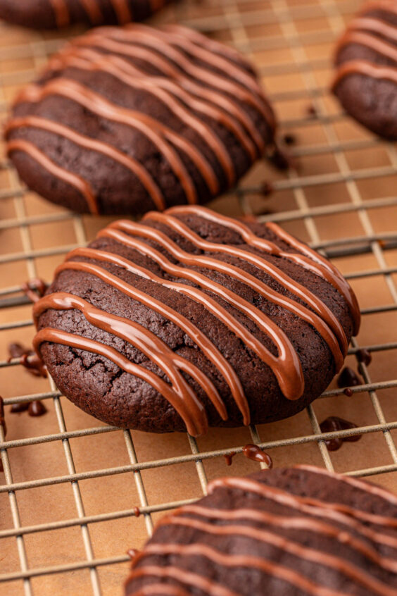 Close up of chocolate cheesecake cookies with chocolate drizzle on a wire rack.