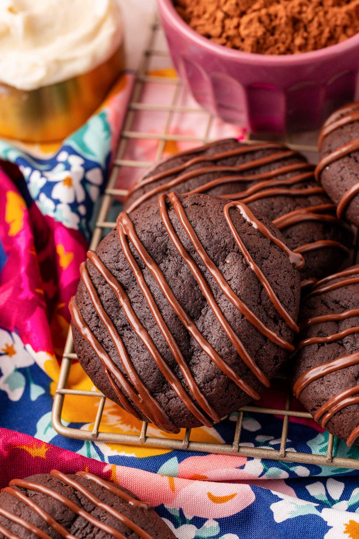 Chocolate cookies with chocolate drizzle on a wire cooling rack.