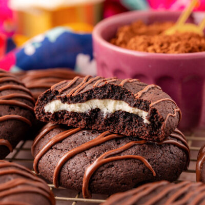 Chocolate cheesecake cookies on a wire rack with one that's been broken in half to show the inside.