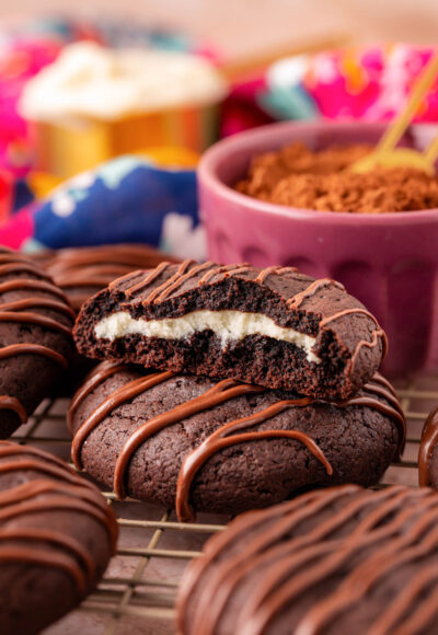 Chocolate cheesecake cookies on a wire rack with one that's been broken in half to show the inside.