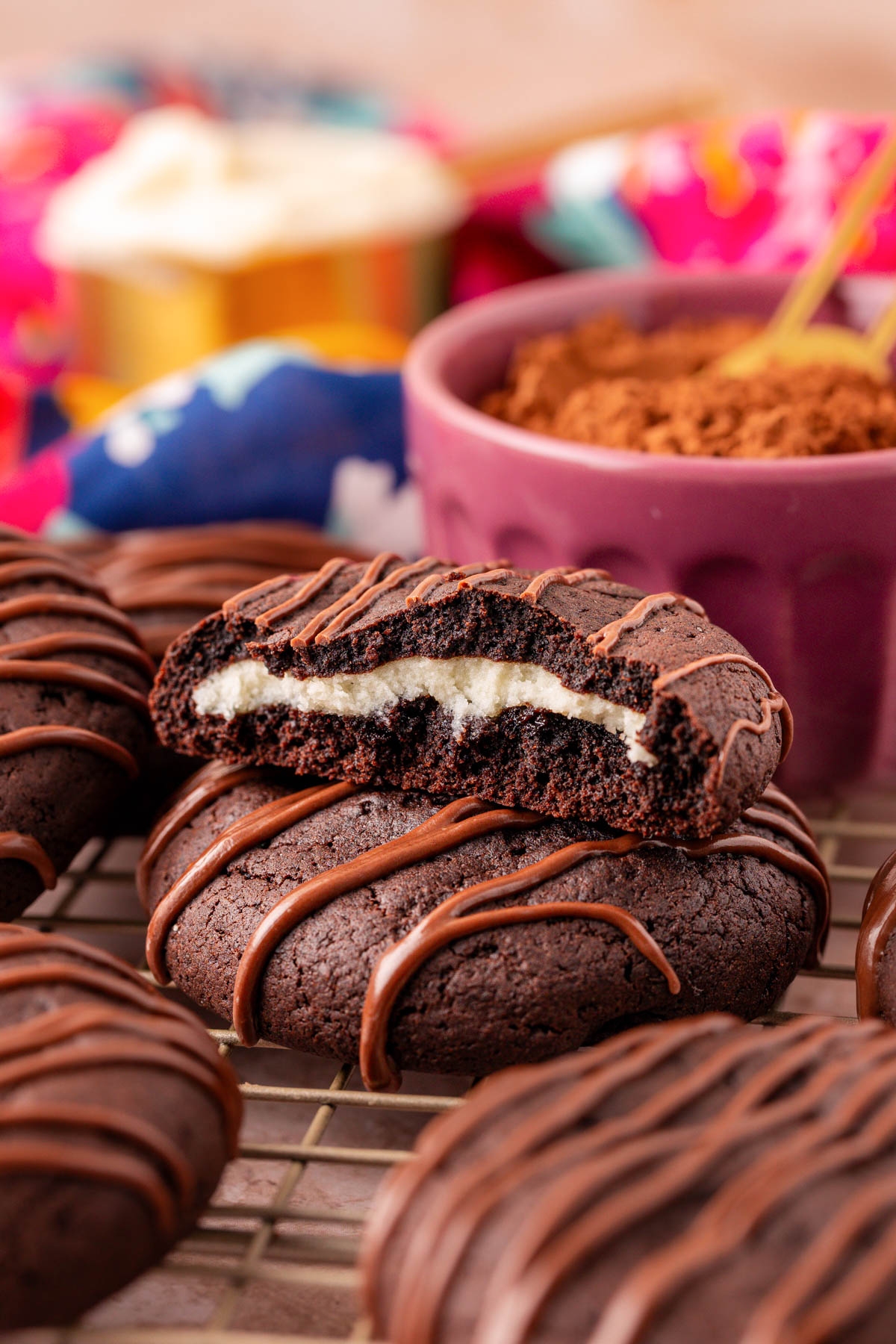 Chocolate cheesecake cookies on a wire rack with one that's been broken in half to show the inside.