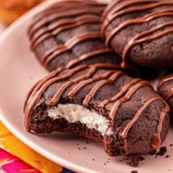 Close up of a chocolate cookie with cream cheese filling on a pink plate with a bite missing.