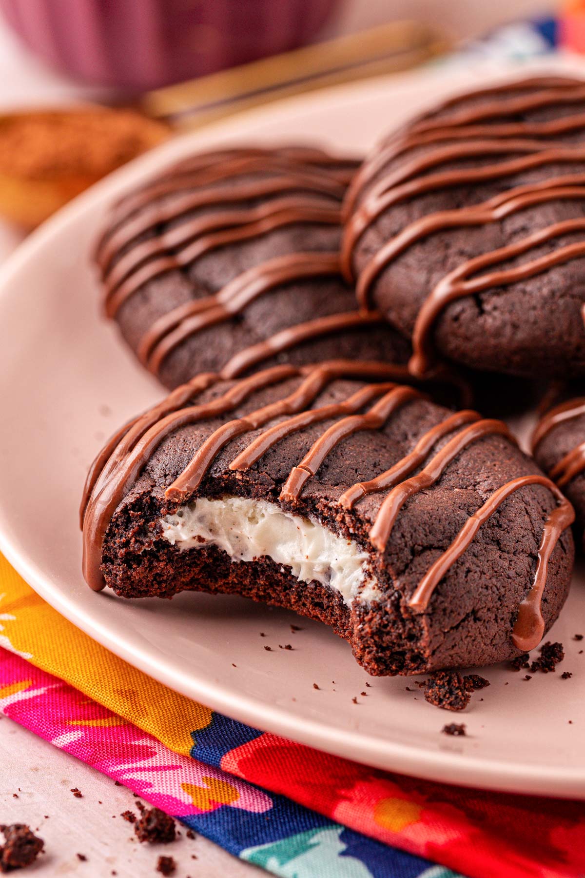 Close up of a chocolate cookie with cream cheese filling on a pink plate with a bite missing.