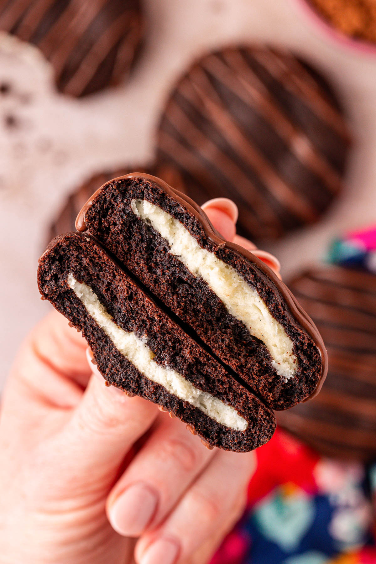 A woman's hand holding a cookie split in half to show the cheesecake filling.