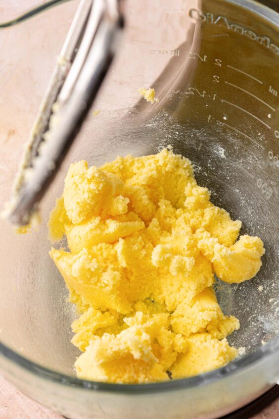 Butter and sugar being creamed in a glass mixing bowl.