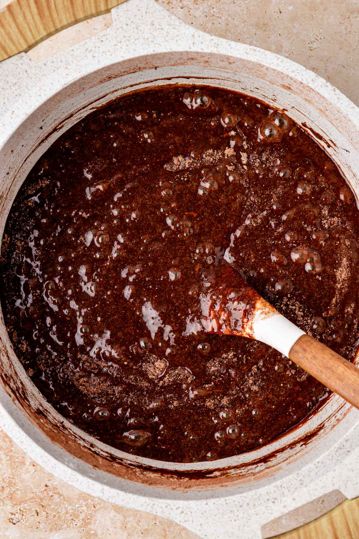 Chocolate chunks being stirred into brownie batter in a pot.