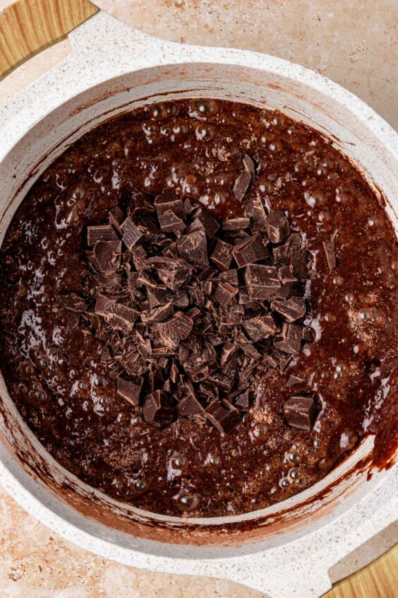 Chopped chocolate resting on top of brownie batter in a pot.