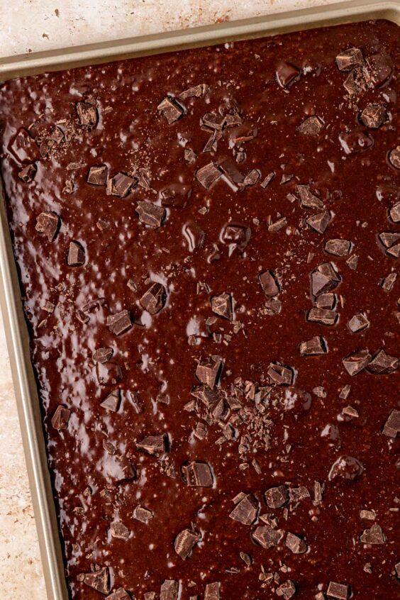 Brownie batter sprinkled with chocolate chunks in a sheet pan.