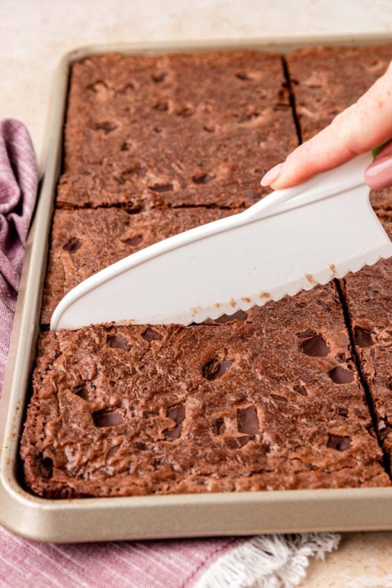 A plastic knife cutting brownies in a sheetpan.