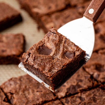 A spatula holding a sheetpan brownie above a pan of brownies.