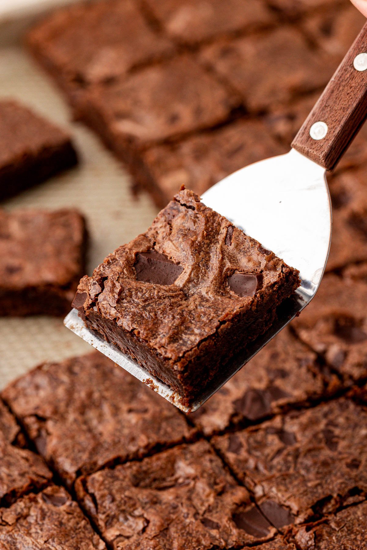 A spatula holding a sheetpan brownie above a pan of brownies.