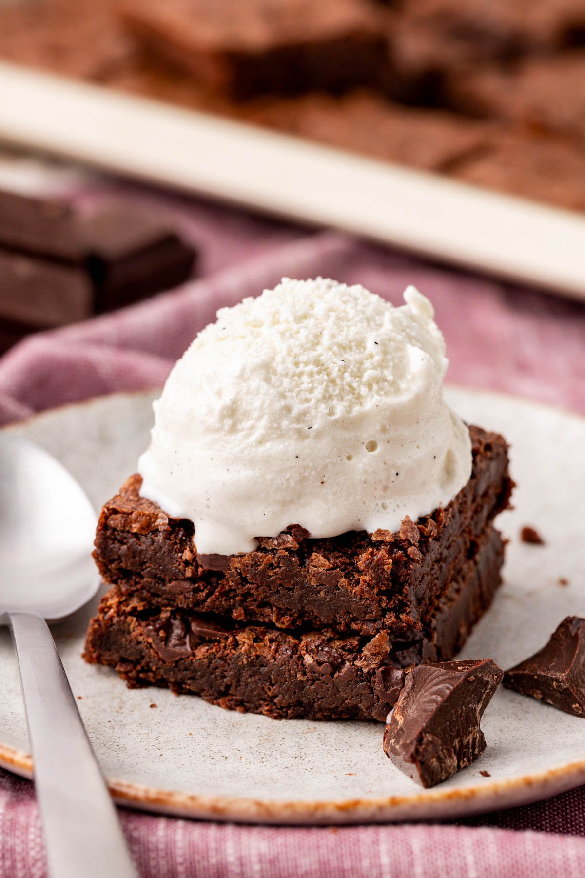 Two thin brownies stacked on a plate and topped with vanilla ice cream.