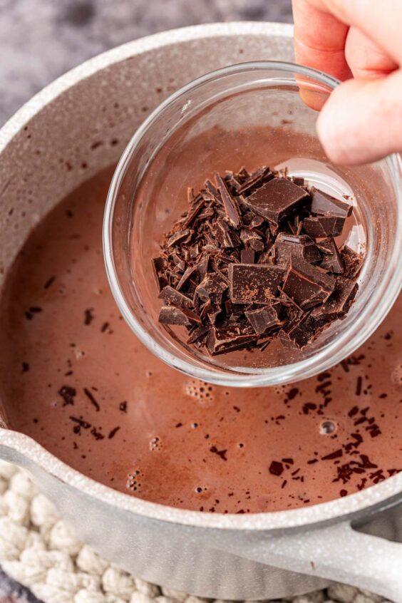 Chopped chocolate being added to a pot of hot chocolate.