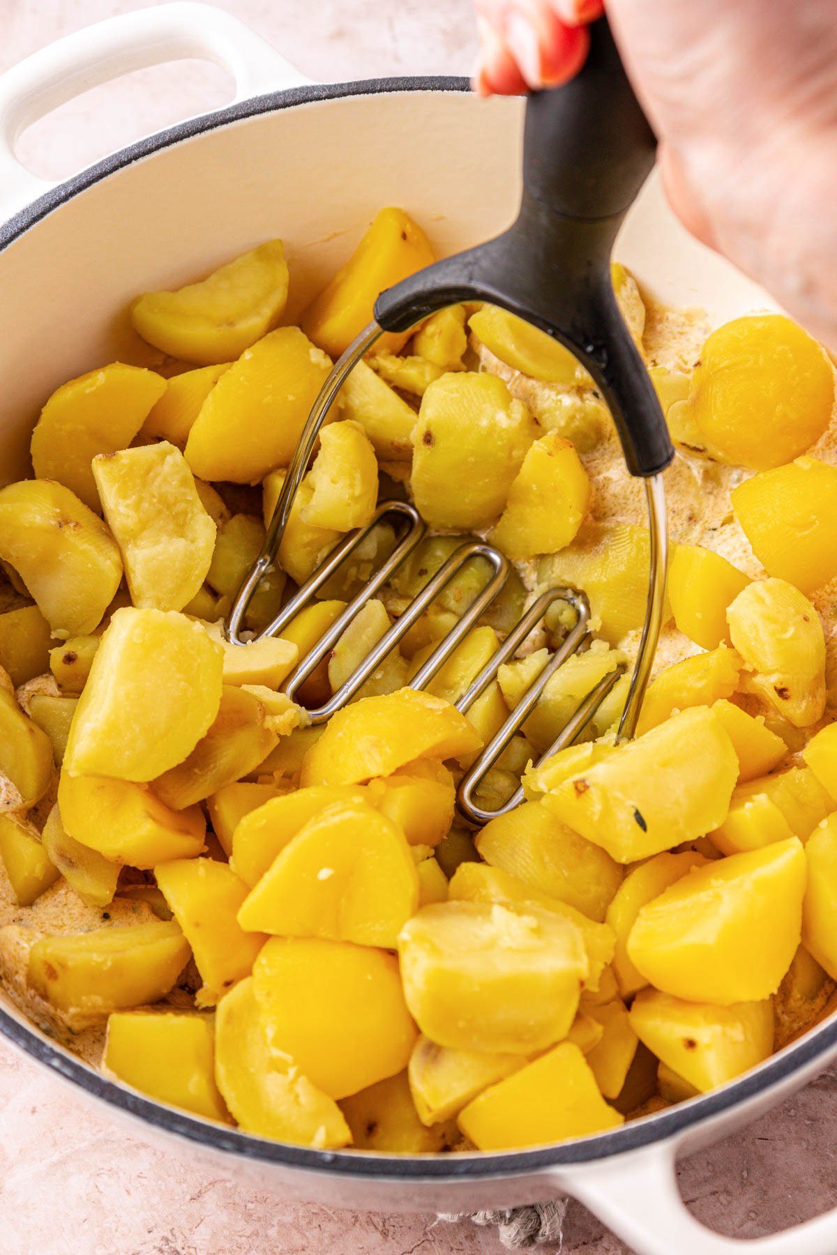 A masher mashing potatoes in a pot.