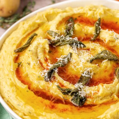 Close up of a bowl of mashed potatoes with brown butter on top.