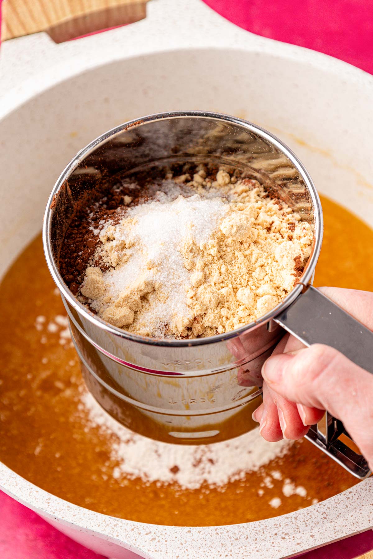 A sifter sifting dry ingredients into a pot to make brownie batter.