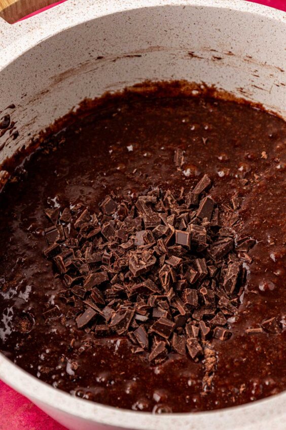 Chocolate chunks being added to brownie batter in a pot.