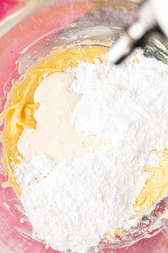 Powdered sugar and cream in a stand mixer bowl ready to be beaten into butter.