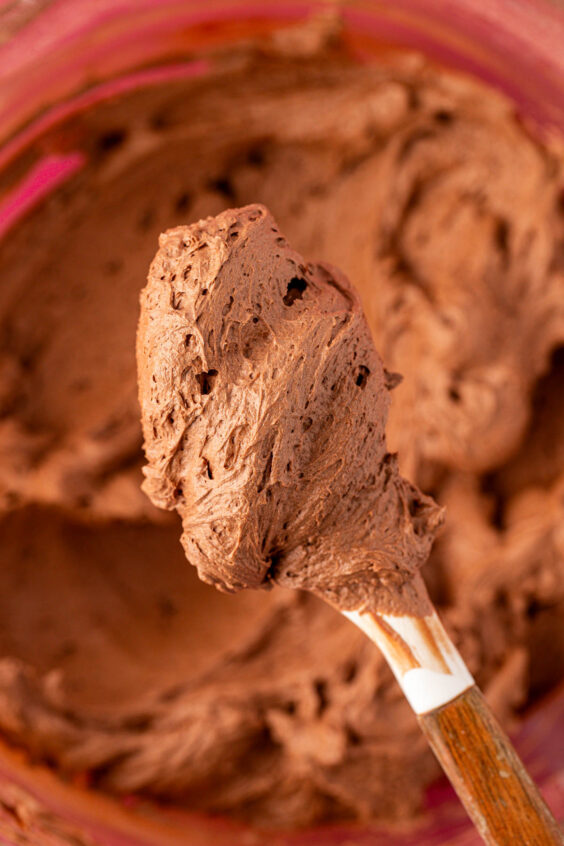 A spatula holding a scoop of whipped chocolate frosting to the camera,