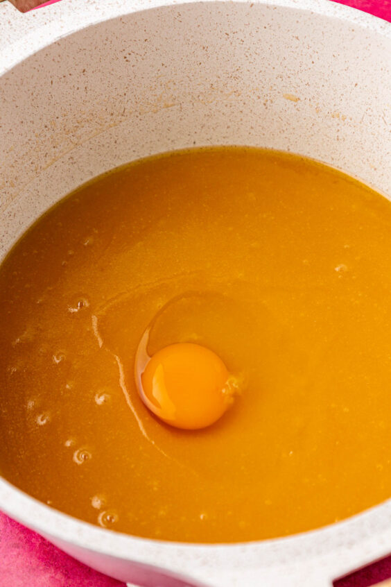 Egg being added to brownie batter in a pot.