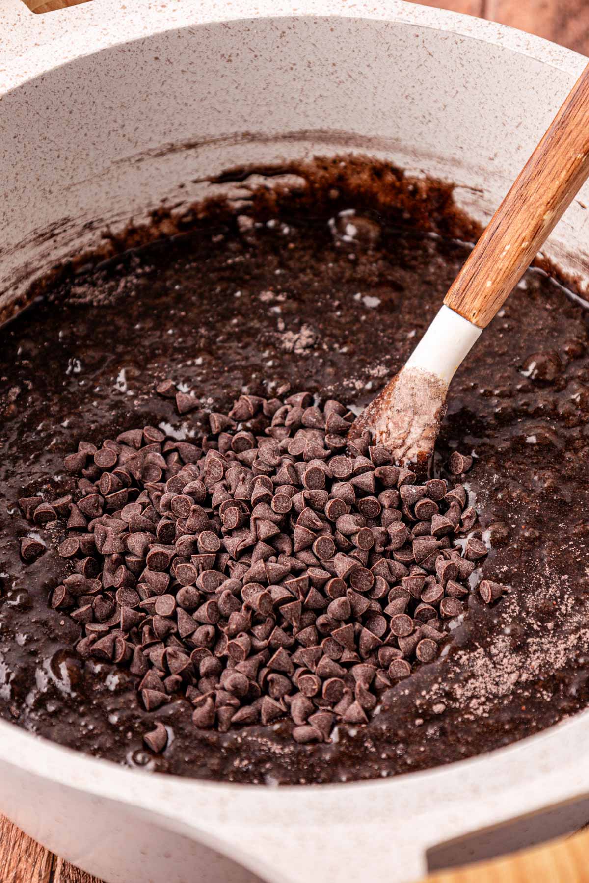 A pot of brownie batter with chocolate chips being folded in.