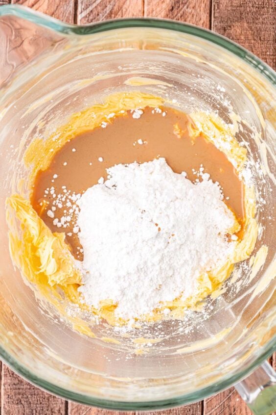 Powdered sugar and Irish cream being added to a mixing bowl with butter.