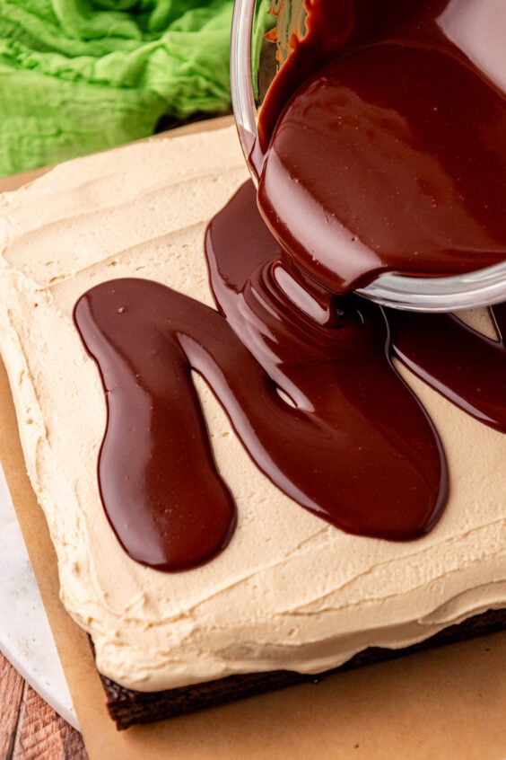 Ganache being poured over the top of frosting on brownies.