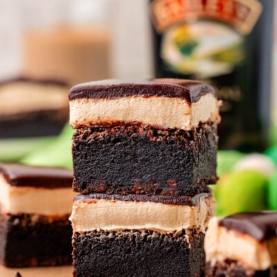 Two brownies with irish cream frosting and ganache topping stacked on a piece of parchment paper.