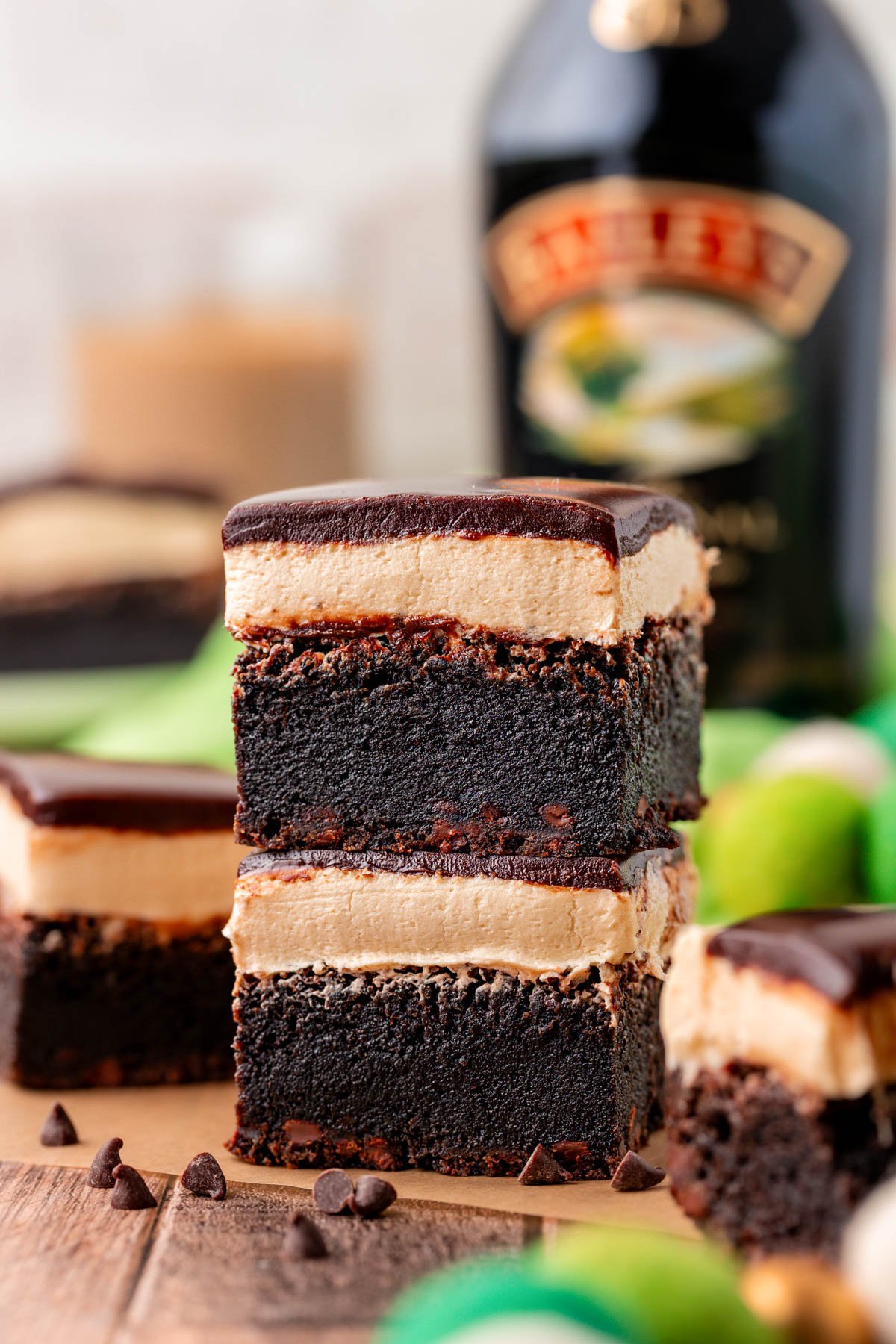 Two brownies with irish cream frosting and ganache topping stacked on a piece of parchment paper.