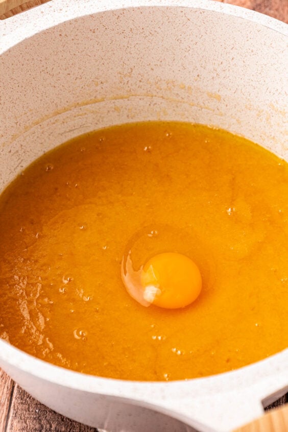 Egg being added to a pot of melted butter and sugar to make brownie batter.