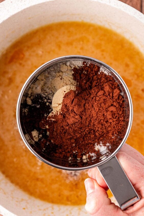 A sifter over a bowl sifting in four, cocoa, and powdered milk.