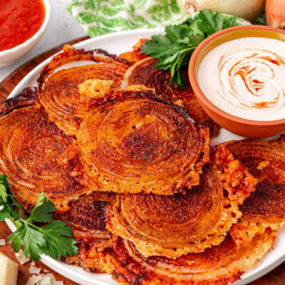 Onion ring chips on a white plate with dipping sauce.