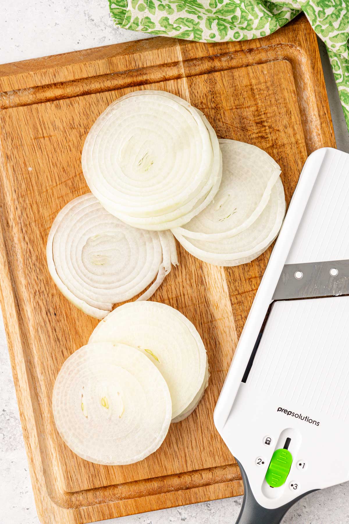 Onions that have been sliced on a mandolin on a cutting board.